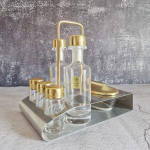 Puede incluir: Un juego de condimentos vintage con botellas y saleros de vidrio transparente con tapas doradas. El juego incluye un soporte de metal con un asa dorada y un plato pequeño. Las botellas tienen etiquetas. Ideal para servir condimentos.