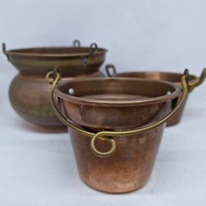 Puede incluir: Tres ollas de cobre con asas de latón. Las ollas están anidadas una dentro de la otra, con la olla más grande en la parte inferior y la olla más pequeña en la parte superior.