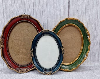 May include: Three oval-shaped picture frames with ornate gold trim. The frames are red, green, and blue.