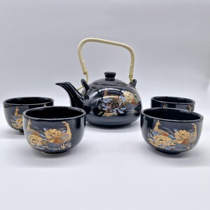 Könnte beinhalten: Schwarzes und goldenes Teeset mit einer Teekanne und vier Tassen. Die Teekanne hat einen Bambusgriff und ein florales Design mit Pfauen. Die Tassen haben ein ähnliches Design.