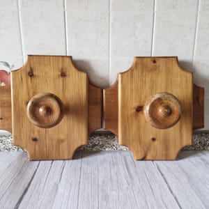 Può includere: Due ganci da parete in legno con un design decorativo. Ogni gancio ha un pomo rotondo e una finitura colorata marrone.