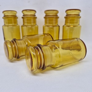 Puede incluir: Seis botellas de vidrio ámbar con tapones de corcho. Las botellas son todas del mismo tamaño y forma, y están dispuestas en una fila.