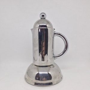May include: A silver stainless steel stovetop coffee maker with a polished finish. The coffee maker has a round base and a tall, cylindrical body with a handle.