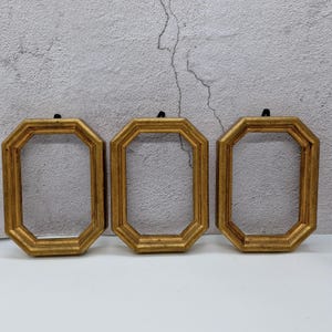 Könnte beinhalten: Drei goldene achteckige Bilderrahmen mit einer strukturierten Oberfläche. Die Rahmen sind in einer Reihe angeordnet, wobei der linke Rahmen leicht vom Zentrum versetzt ist.