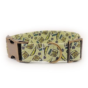Peut inclure: Un collier pour chien avec un fond vert clair orné de bocaux de cornichons et de tranches. Il est doté d'une boucle en métal de couleur bronze et d'un anneau en D assorti. Le nom de la marque "SANDY PAWS COLLAR CO." est imprimé sur le côté.