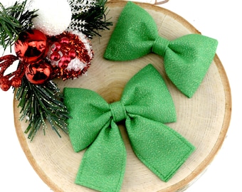 Puede incluir: Dos pajaritas de brillo verde sobre una superficie de madera. Las pajaritas están hechas de una tela verde brillante y están atadas en forma de lazo clásico.