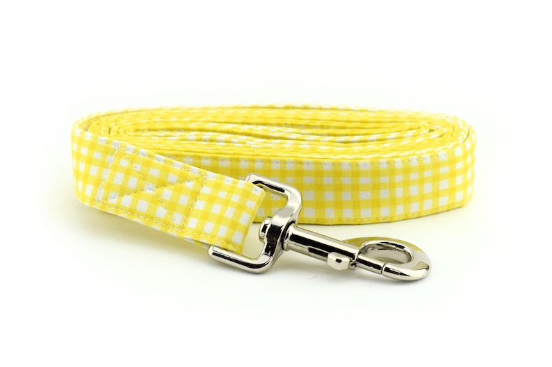 Op de afbeelding: Een gele en witte gingham hondenriem met een zilveren clip.