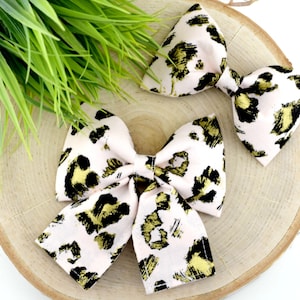 May include: Two pink fabric hair bows with a gold and black leopard print pattern.