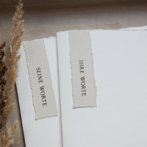 Peut inclure: Deux cartes blanches aux bords d&eacute;chir&eacute;s, chacune avec une &eacute;tiquette beige. L'&eacute;tiquette de gauche indique "SEINE WORTE" et l'&eacute;tiquette de droite indique "IHRE WORTE".