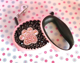 May include: Pink retractable dog leash with a black paw print design made of rhinestones.
