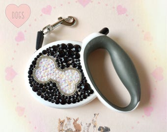 May include: White retractable dog leash with a black and white rhinestone design of a bone. The leash has a gray handle.