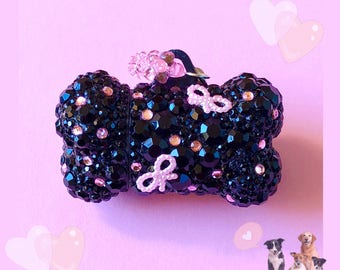 May include: Black bone-shaped charm with pink rhinestones and bows. The charm is covered in small black crystals.