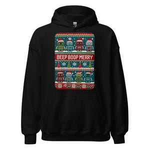 May include: A black hooded sweatshirt featuring a rectangular graphic print with rows of colorful robots wearing Santa hats, small Christmas trees, and snowflakes. The text BEEP BOOP MERRY is printed in white across a red horizontal band.