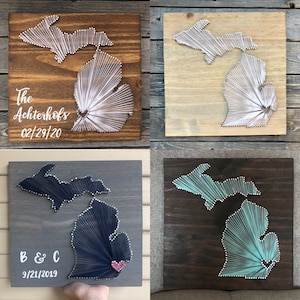 May include: Four wooden plaques featuring string art of the state of Michigan. The plaques are stained in various colors, including brown, gray, and teal. Some plaques include names and dates, such as "The Achterhofs 02/29/20" and "B & C 9/21/2019".