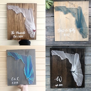 May include: Four wooden Florida state string art pieces. Each features the state outline with string, in various colors, on a stained wooden board. Some include names and dates: "The Persauds Est. 2.18.19", "Scott & Kelly 4.1.17", "C & L 8-31-19", and "W est. 2019".