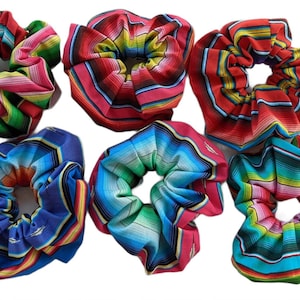May include: Six colorful hair scrunchies with a Mexican serape pattern. The scrunchies are made of fabric and have a gathered look. The colors include red, green, blue, yellow, and white.