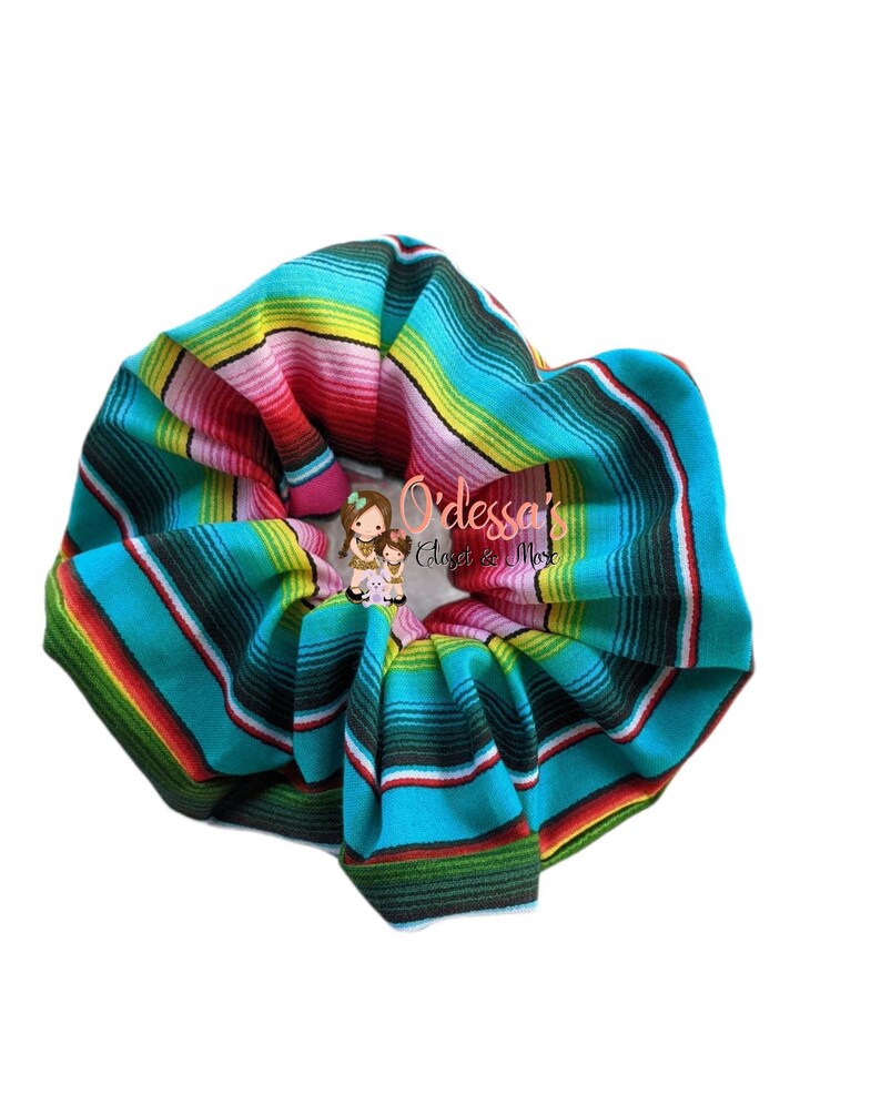 May include: A turquoise, green, yellow, red, and black striped scrunchie. The scrunchie is made of fabric and has a  "O'dessa's Closet & More" logo.