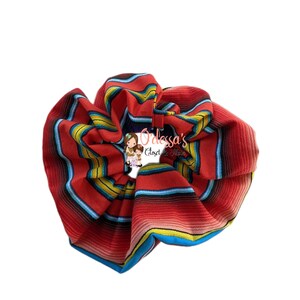 May include: Red, blue, yellow, and white striped scrunchie. The scrunchie is made of fabric and is in the shape of a large circle.
