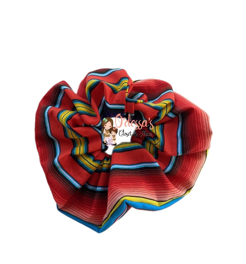 May include: Red, blue, yellow, and white striped scrunchie. The scrunchie is made of fabric and is in the shape of a large circle.