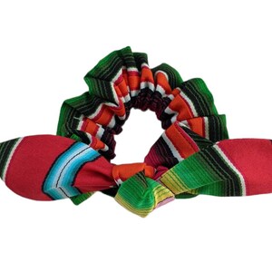 Puede incluir: Una colorida scrunchie con lazo, con un vibrante estampado de rayas en rojo, verde, naranja y azul. La scrunchie est&aacute; dise&ntilde;ada con un estilo textil tejido tradicional, perfecta para a&ntilde;adir un toque de color a cualquier peinado.