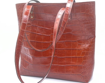 May include: A brown leather tote bag with a crocodile embossed pattern and two long straps.
