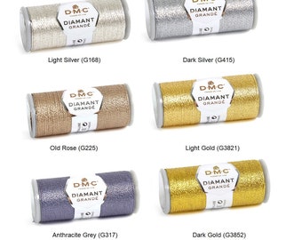 Könnte beinhalten: Sechs Spulen DMC Diamant Grande Stickgarn in verschiedenen Metallic-Farben: Hell Silber, Dunkel Silber, Altrosa, Hell Gold, Anthrazit Grau und Dunkel Gold. Jede Spule trägt das DMC-Logo und den Text "Diamant Grande" aufgedruckt.