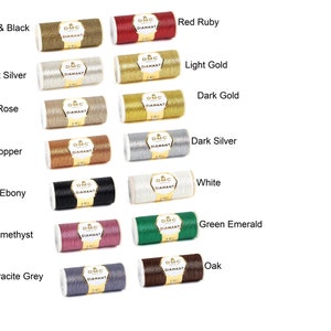 Könnte beinhalten: Eine Sammlung von 10 Spulen DMC Diamant Stickgarn in verschiedenen Farben, darunter Gold, Silber, Rot, Grün, Weiß und Schwarz. Jede Spule ist mit dem DMC Diamant Logo und dem Farbnamen gekennzeichnet.