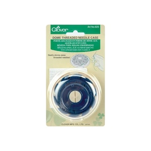May include: A clear plastic dome-shaped needle case with a blue threaded needle holder inside. The case is labeled "Dome Threaded Needle Case" and "Clover" with a clover leaf logo. The packaging also includes instructions in multiple languages.