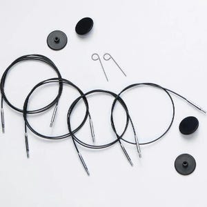 May include: Set of four black circular knitting needles with silver tips and two black end caps. The needles are arranged in a circle with the end caps on either side. There are also two silver metal stitch holders.