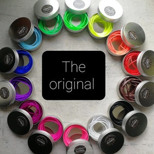 May include: A collection of small, round metal tins, each containing a different color of hair ties. The tins are silver with a black label that says "BARBER". The text "The original" is displayed on a black background.