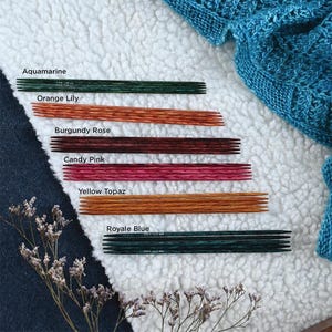 Peut inclure: Un ensemble de six paires d'aiguilles à tricoter de différentes couleurs, notamment aigue-marine, lys orange, rose bourgogne, rose bonbon, topaze jaune et bleu royal. Les aiguilles sont disposées sur une surface blanche et moelleuse.