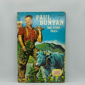 May include: A vintage book cover featuring a cartoon illustration of Paul Bunyan, a giant lumberjack, holding an axe and walking with a blue ox. The book title is "Paul Bunyan and Other Tales" and the cover is blue with white text. The book is a Golden Reading Adventure.