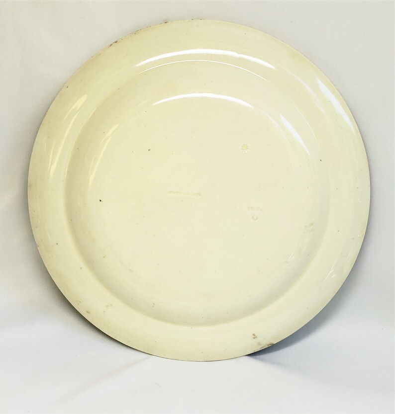 May include: The back of a white ceramic plate with a raised rim. The plate has a simple design and is in good condition.