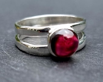 May include: A silver ring with a deep red gemstone set in a double band.