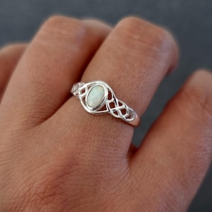Może przedstawiać: Srebrny pierścionek z białym opalem osadzonym w celtyckim wzorze węzła.