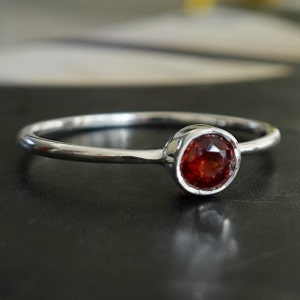 May include: A simple silver ring with a single, round, red gemstone.