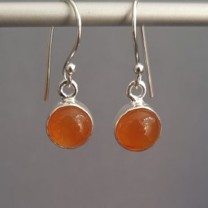 Könnte beinhalten: Ein Paar silberne Ohrhänger mit orangefarbenen Karneol-Edelsteinen. Die Ohrringe haben ein schlichtes Design und sind perfekt für den Alltag.