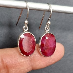 Könnte beinhalten: Ein Paar silberne Ohrhänger mit ovalen roten Rubin-Edelsteinen.