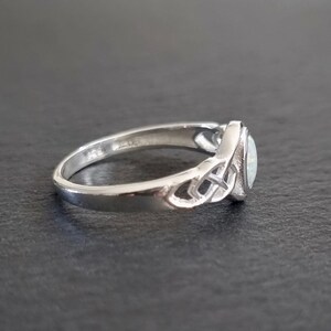 May include: A silver ring with a white opal stone set in a Celtic knot design.