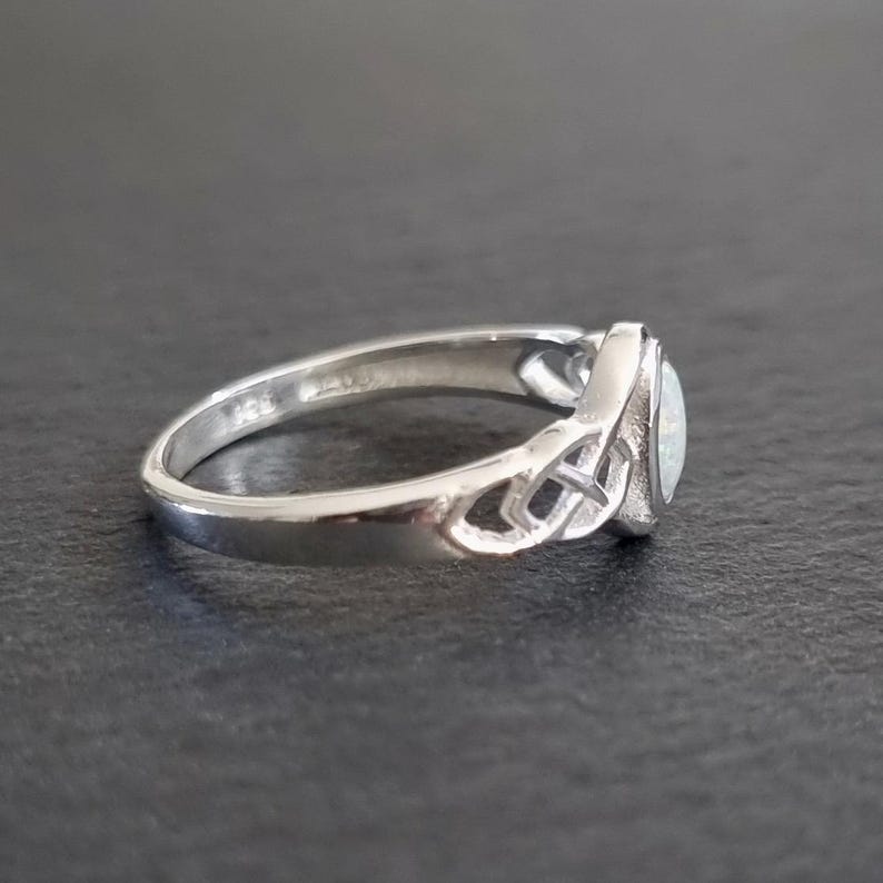 May include: A silver ring with a white opal stone set in a Celtic knot design.