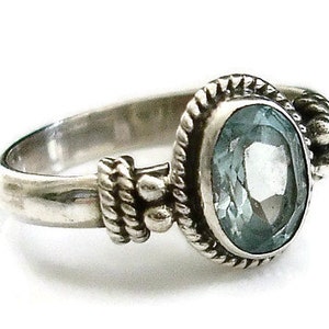 May include: A silver ring with an oval-shaped blue gemstone set in a decorative bezel. The ring has a textured band with small beads.