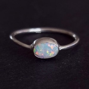 May include: A silver ring featuring a white opal gemstone. The opal has a rainbow sheen.