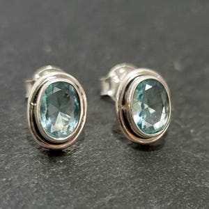 Può includere: Un paio di orecchini a lobo in argento con pietre di topazio blu ovali.