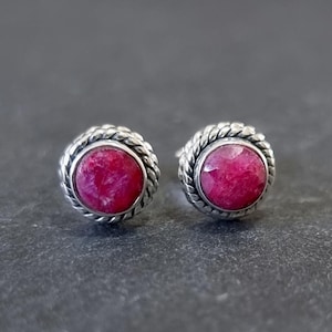 Può includere: Un paio di orecchini a lobo in argento con una pietra preziosa rosa in ogni orecchino. Le pietre preziose sono incastonate in un design a corda.