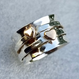 May include: A silver spinning ring with three gold hearts. The ring is made of multiple bands that spin around each other.