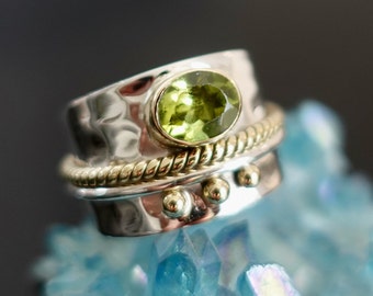 May include: A silver and gold ring with a green gemstone. The ring has a textured band and a rope-like design.