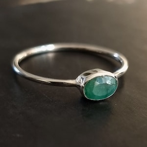 May include: A silver ring set with a green oval emerald gemstone.
