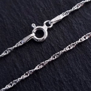 Può includere: Una collana a catena d'argento con una chiusura a moschettone. La catena è un design delicato a corda intrecciata. La chiusura è contrassegnata con "925" e "C.Z.O."