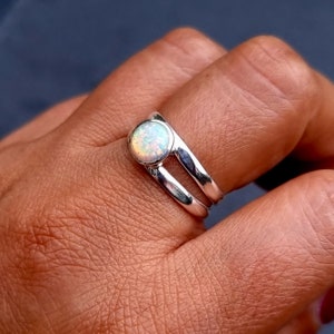 Könnte beinhalten: Ein silberner Ring mit einem weißen Opal-Edelstein. Der Ring hat ein Doppelband-Design.