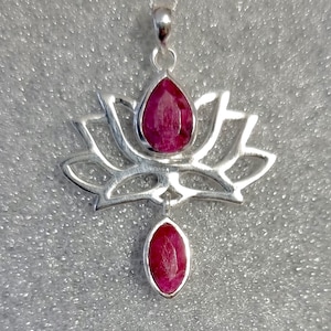 May include: A silver lotus pendant featuring two red ruby gemstones. The pendant is delicately crafted with intricate details.